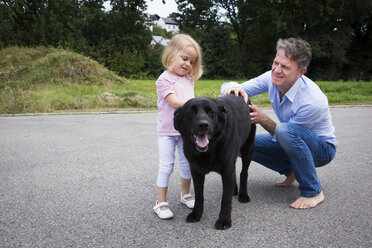 Father and daughter petting dog in garden - JTLF00119