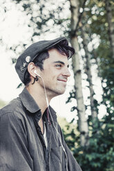 Lächelnder junger Mann mit Mütze, der mit Kopfhörern Musik hört - DWIF00798