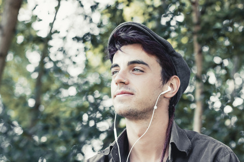 Porträt eines lächelnden jungen Mannes mit Mütze, der mit Kopfhörern Musik hört, lizenzfreies Stockfoto