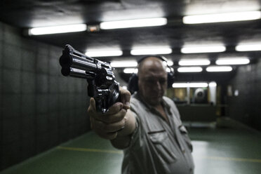 Mann mit Gehörschutz beim Zielen mit einem Revolver in einer Schießhalle - ABZF01276