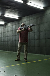 Mann beim Zielen mit einer taktischen Waffe in einer Schießhalle - ABZF01284