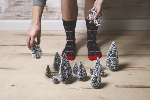 Young man wearing winter socks placing Christmas tree decoration on the floor - RTBF00394