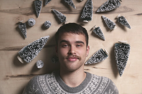 Young man lying on the floor surrounded by Christmas tree decoration - RTBF00396