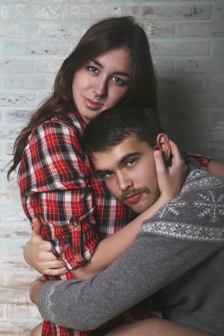 Porträt eines jungen Paares, das sich an einer Backsteinmauer umarmt, lizenzfreies Stockfoto