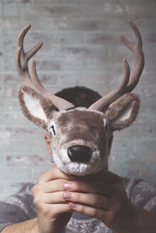 Young man holding artificial deer head in front of his face - RTBF00403
