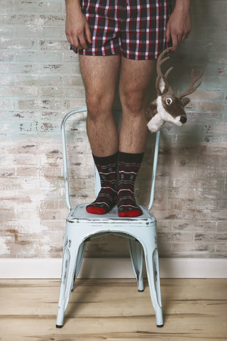 Mann steht auf einem Stuhl und hält einen künstlichen Hirschkopf, lizenzfreies Stockfoto