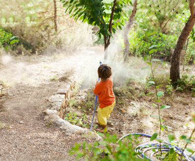 Rückansicht eines kleinen Jungen, der mit einem Gartenschlauch spielt - VABF00778