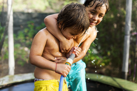 Zwei kleine Brüder spielen mit einem Wasserschlauch auf einem Trampolin, lizenzfreies Stockfoto