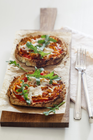 Zwei hausgemachte glutenfreie Mini-Pizzen mit Blumenkohl, Kürbis und Rucola auf Holzbrett, lizenzfreies Stockfoto