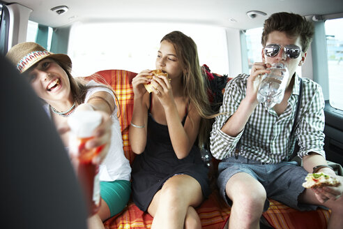 Drei Freunde im Teenageralter essen einen Snack im Auto - FSF00529