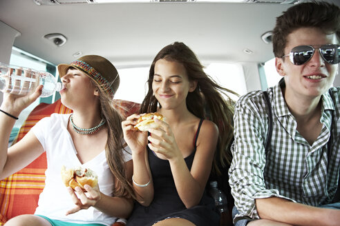 Drei Freunde im Teenageralter essen einen Snack im Auto - FSF00531