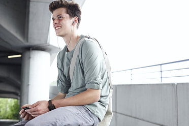 Smiling teenage boy with cell phone and earbuds outdoors - FSF00535