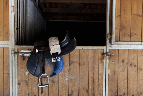 Saddle hanging on door of horse stable - VABF00790