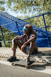 Junge Frau mit Skateboard auf einer Brücke sitzend - KIJF00820