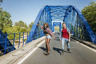 Junges Paar mit Inline-Skates und Skateboard fährt auf einer Brücke - KIJF00821