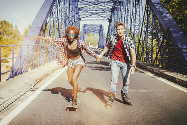 Junges Paar mit Inline-Skates und Skateboard fährt auf einer Brücke - KIJF00822