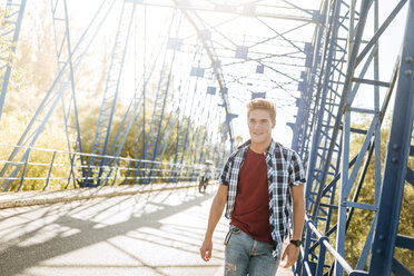 Smiling young man walking on a bridge - KIJF00823