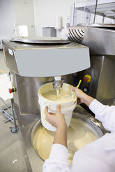 Frau pflückt weiße Schokolade mit einem Eimer aus einer Maschine in einer Schokoladenfabrik - ABZF01290