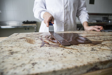 Frau temperiert geschmolzene Schokolade auf einer Marmorfläche - ABZF01310