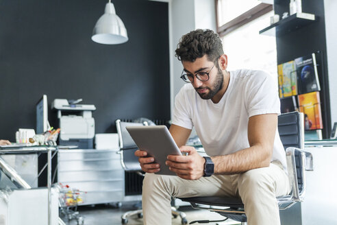 Junger Mann schaut auf Tablet in einem modernen Büro - TCF05109