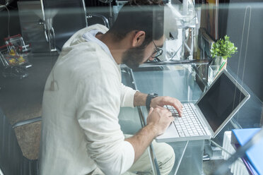 Junger Mann arbeitet mit Laptop am Schreibtisch in einem modernen Büro - TCF05111