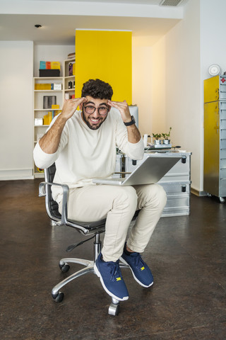 Young man with laptop in a modern office pulling funny faces stock photo