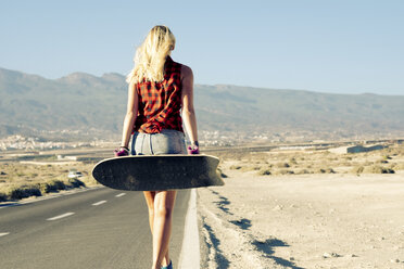 Spanien, Teneriffa, blonde junge Skaterin mit Skateboard läuft auf der Straße - SIPF00894