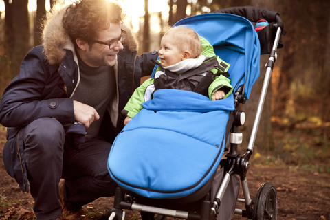 Vater lächelt Sohn im Buggy im Wald an, lizenzfreies Stockfoto