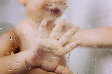 Hand eines kleinen Jungen gegen nasse Glasscheibe in der Dusche - MFF03386