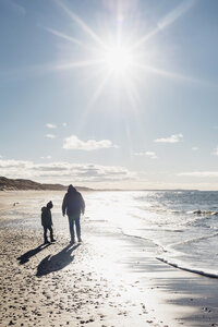 Dänemark, Hirtshals, Vater und Sohn spazieren am Strand im Gegenlicht - MJF02066