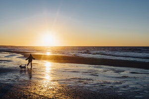 Dänemark, Nordjütland, Junge mit Hund am Strand bei Sonnenuntergang - MJF02080