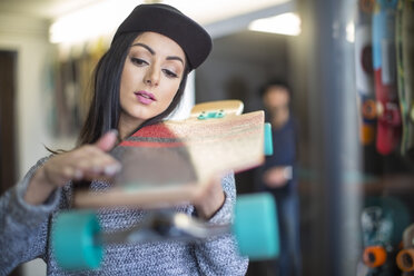 Junge Frau begutachtet Skateboard in einem Geschäft - ZEF10445