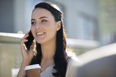 Lächelnde Frau mit Kaffee zum Mitnehmen, die mit ihrem Handy telefoniert - ZEF10494