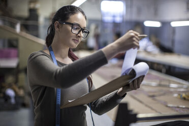 Modedesignerin in einer Bekleidungsfabrik, die ihre Arbeit am Klemmbrett kontrolliert - ZEF10537