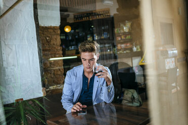 Junger Mann sitzt in einer Bar und schaut auf sein Handy - KIJF00841