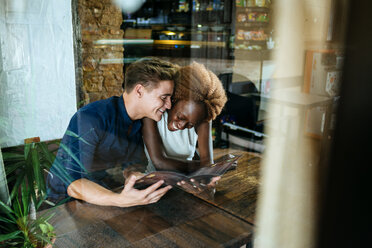 Young couple looking at a restaurant menu seen through a window - KIJF00846