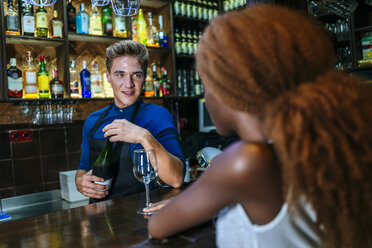 Waiter serving wine to a woman at the bar - KIJF00850