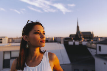 Österreich, Wien, junge Frau entspannt sich bei Sonnenuntergang auf einer Dachterrasse mit Stephansdom im Hintergrund - AIF00372