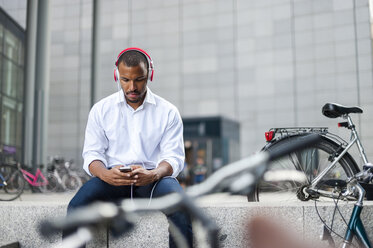 Businessman listening music with headphones looking at smartphone - DIGF01329