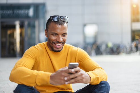 Smiling man wearing yellow pullover looking at cell phone - DIGF01345