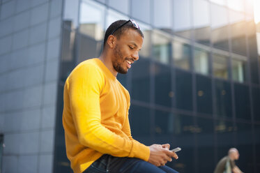 Portrait of smiling man wearing yellow pullover text messaging - DIGF01348