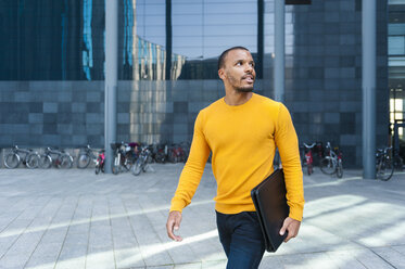 Young man with file wearing yellow pullover watching something - DIGF01350