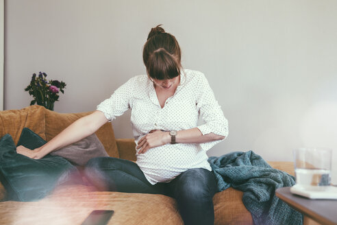 Expectant mother timing her contractions while sitting on couch at home - MFF03389