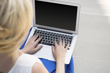 Back view of blond businesswoman sitting on stairs using laptop, partial view - GDF01122