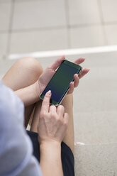 Geschäftsfrau sitzt auf einer Treppe und benutzt ein Smartphone, Teilansicht - GDF01125