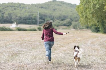 Rückenansicht einer Frau, die mit ihrem Hund auf einer Wiese läuft - SKCF00214