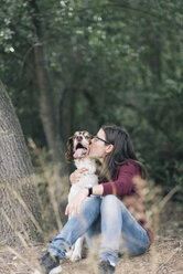 Woman sitting on forest ground kissing her dog - SKCF00216