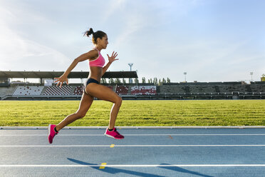 Female athlete taking position on her marks to start off the run. Side view  of female runner sitting at the start line on running track on a black  background. stock photo