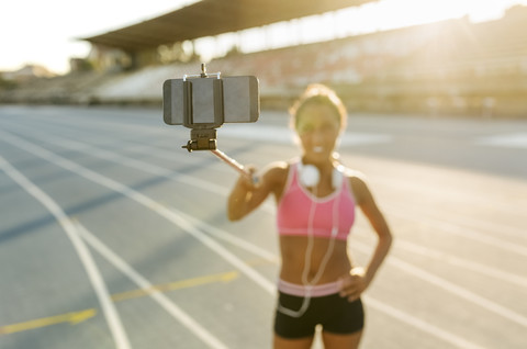 Weibliche Athletin macht Selfies im Stadion, hält Selfie-Stick, lizenzfreies Stockfoto