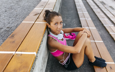 Female athlete taking a break, sitting in stadium - MGOF02515